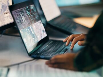 Hands typing, laptop and closeup on table of military intelligence, map and research on internet. C