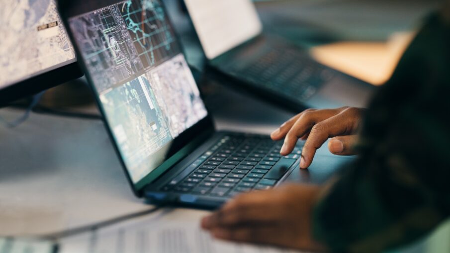 Hands typing, laptop and closeup on table of military intelligence, map and research on internet. C